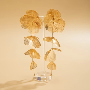 Détail de grandes boucles d'oreilles fleurs dorées avec texture métallique brossée