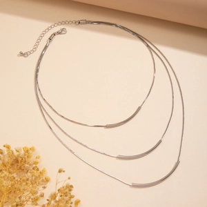 Close-up of triple-layered silver snake chain necklace with curved metal tube pendants
