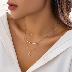 Detail of layered gold necklaces with tube and crescent pendants on white shirt