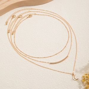 Detailed view of triple-layered gold necklaces with beads, tube, and crescent moon pendants