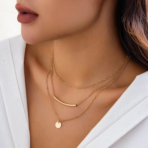 Close-up of three-layered gold necklaces with tube and disc pendants on a white shirt