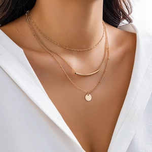 Detailed view of layered gold necklace featuring minimalist tubes and round pendant on model