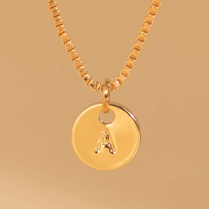 Close-up of gold box chain necklace featuring a round coin pendant with embossed letter A