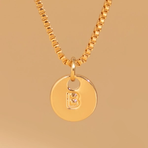Macro detail of gold-plated round pendant necklace with embossed capital letter B