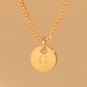 Close-up of golden round pendant with letter C engraving on a delicate box chain