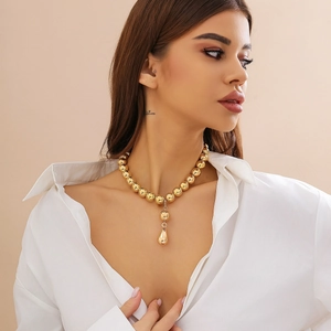 Dettaglio della collana girocollo con grandi perle dorate e ciondolo a goccia su modella