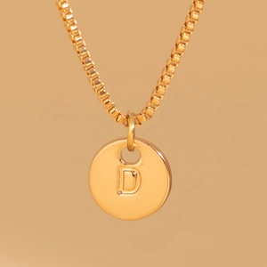 Macro shot of gold-plated round pendant with engraved letter D on a box chain