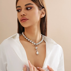 Dettaglio della collana di perle d'argento con grande ciondolo a goccia su camicia bianca