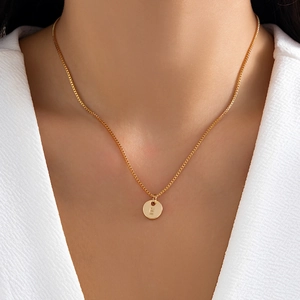 Close-up of golden round pendant with engraved letter E on a box chain for women
