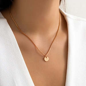Detail of a gold letter F pendant necklace on model showing delicate square chain