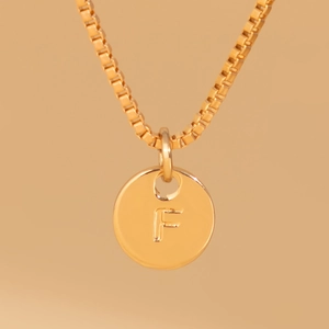 Macro shot of gold box chain and round pendant featuring engraved capital letter F