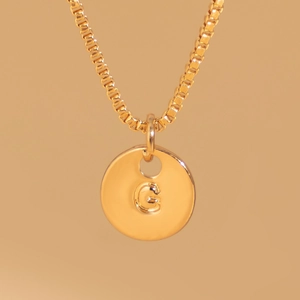 Macro view of polished gold round pendant featuring a 3D embossed letter G and thin chain
