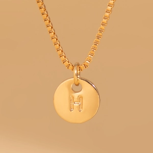 Macro detail of gold round coin pendant with embossed letter H on a box chain