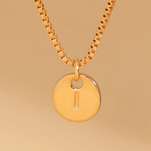 Close-up of gold box chain necklace featuring a round pendant with engraved letter I