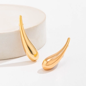 Gros plan de boucles d'oreilles gouttes dorées avec finition miroir sur support en pierre