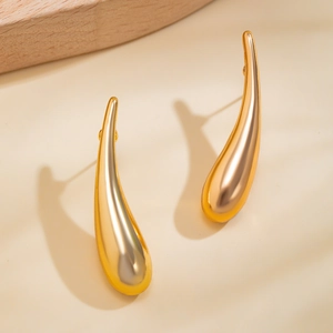 Vue détaillée de boucles d'oreilles goutte dorées sur fond beige chaleureux
