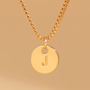 Detailed macro view of golden letter J engraved round pendant on a box chain