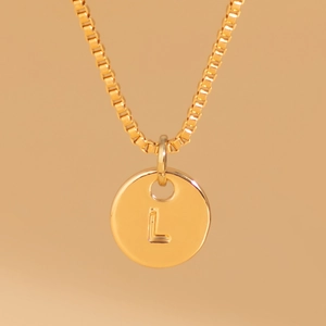 Detail of a gold box chain necklace featuring a round pendant with engraved letter L