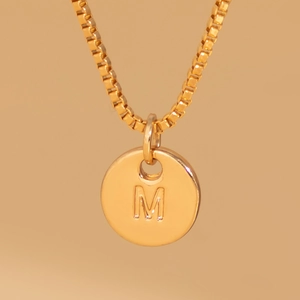 Macro detail of gold round pendant with engraved M letter on a classic box chain