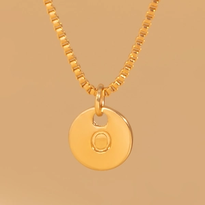 Macro detail of gold box chain and engraved letter O pendant on warm background