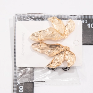Gouden bloembladvormige oorbellen met metalen textuur getoond naast een meetlat