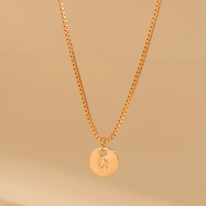 Macro shot of gold box chain necklace featuring a round pendant engraved with letter Q