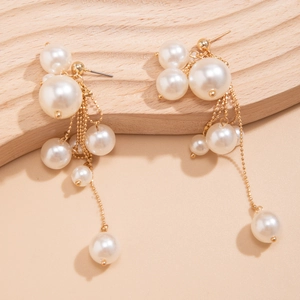 Détail de boucles d'oreilles à pompon avec perles blanches et chaînes à billes dorées