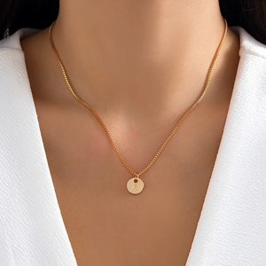 Close-up of minimalist gold necklace with a round pendant engraved with the letter R