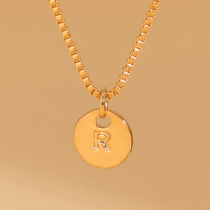 Detailed close-up of a gold-plated round disk pendant with an engraved letter R