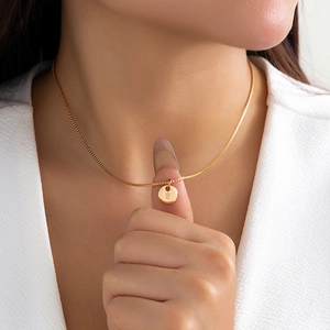 Detailed view of a gold circular pendant with engraved S letter on a box chain