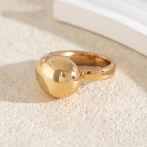 Detailed view of an oversized golden sphere ring with a polished mirror finish and open band