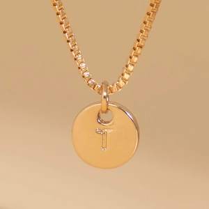 Detailed macro shot of a gold box chain necklace with a round initial T pendant