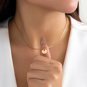 Close-up of golden letter U round pendant necklace on model with refined box chain detail