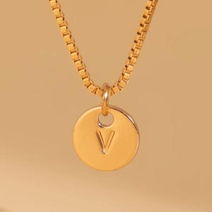 Macro detail of golden round pendant featuring letter V and delicate box chain necklace