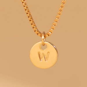Macro shot of gold box chain necklace with a minimalist engraved letter W round pendant