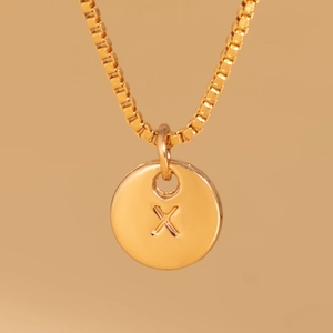 Macro shot of gold box chain necklace featuring an engraved round letter X pendant