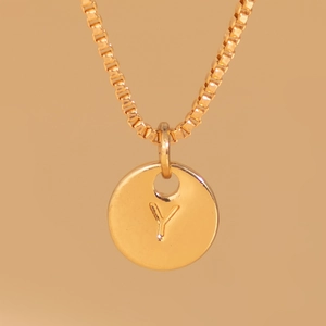 Macro view of gold box chain and engraved letter Y coin pendant on warm background