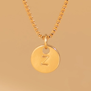 Detail of a gold box chain necklace with a circular pendant engraved with the letter Z