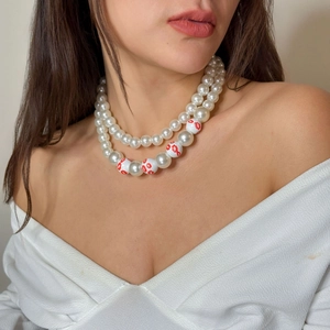 Detail einer zweilagigen Perlenkette mit roten Lippenmustern auf weißen Perlen