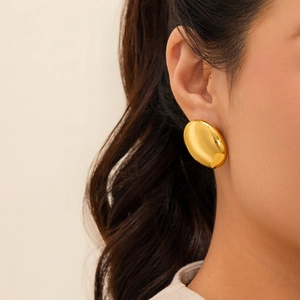 Close-up of a model wearing large gold oval earrings with a smooth polished metallic finish
