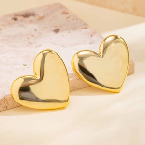 Close-up of chunky gold heart earrings with a polished finish on a stone background