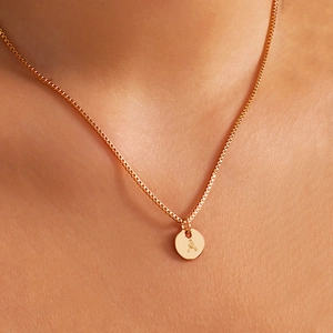 Minimalist gold necklace with a round pendant engraved with the letter A worn by a model