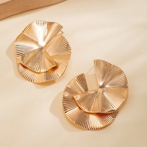 Detailed view of gold geometric earrings with radiant textured folds on a beige backdrop