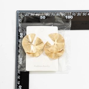 Detail view of large gold pleated fan earrings showing dimensions with a ruler