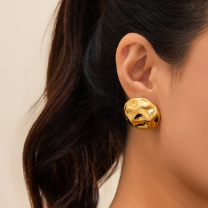 Close-up of golden irregular hammered geometric stud earrings on a model's ear