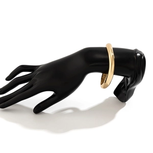Bracciale rigido in oro lucido su modello di mano nera con trama metallica stropicciata
