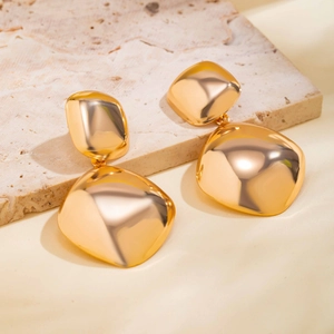 Macro shot of large golden geometric pendant earrings on a textured stone surface
