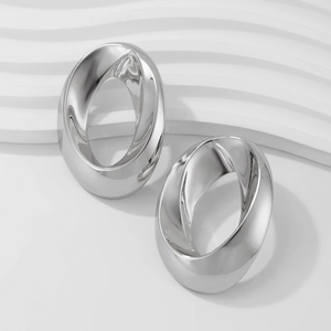 Dettaglio di orecchini ovali in argento lucido su un supporto bianco con texture
