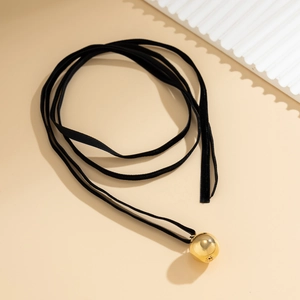 Minimalist black ribbon necklace featuring a polished gold sphere pendant on beige background