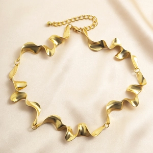 Detalle de collar dorado con diseño de metal líquido en espiral sobre fondo de seda